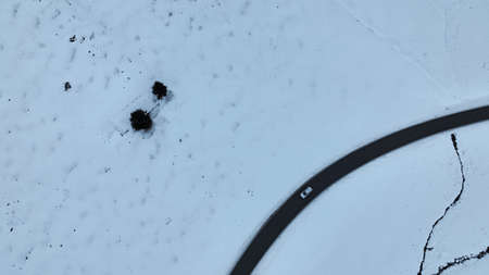 Aerial drone shot of a road with a moving car in a lonely winter landscapeの写真素材