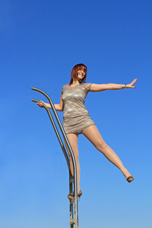 A young woman in a dress stands high up on a ladder and stretches out one arm and one legの写真素材