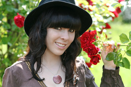 A smiling dark-haired young woman with a hat next to red rosesの写真素材