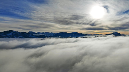 Drone shot in winter with fog in the valley and sun in the mountainsの写真素材