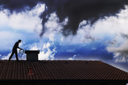A chimney sweep cleans the chimney on a rooftop in front of a dramatic sky sceneの写真素材