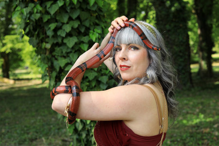 A woman holds a red and black snake over her head