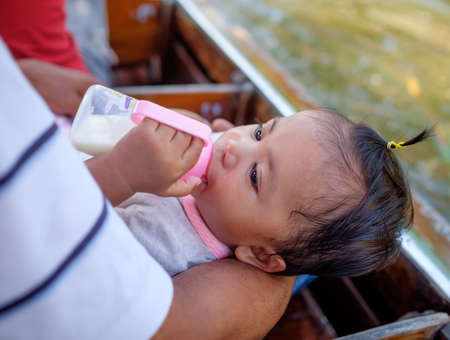 thai baby drink milk on row boat along river with familyの写真素材