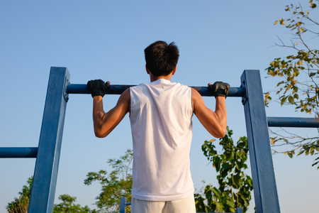 fitness ,sport, exercise, training and lifestyle concept - one youngman doing pull ups on horizontal bar outdoors in eveningの写真素材