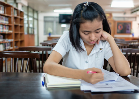 selective focus on thai young adult woman student in uniform reading a book in library with stressの写真素材
