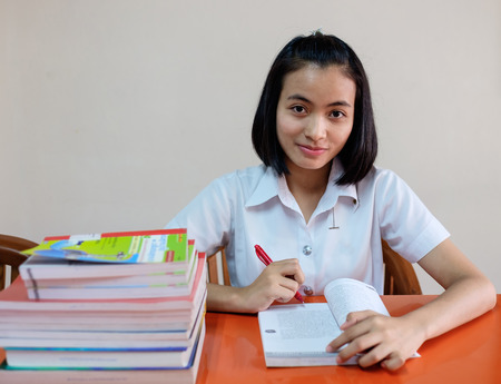 selective focus on thai young woman student in uniform is reading a book, sitting with tableの写真素材