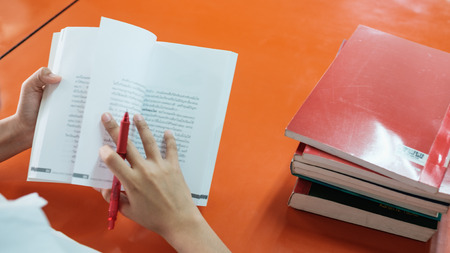 blurred book page, selective focus on book hold by girl student. sitting near table reading books...