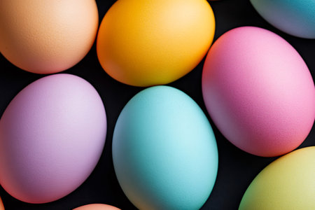 Many colorful pastel easter eggs are lying on a black background, creating a beautiful patternの素材