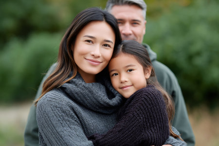 Mixed race mother and daughter smiling, father in background, representing family bonding outdoorsの素材
