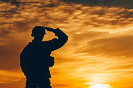 Soldier in uniform saluting, featuring a strong silhouette against a vibrant orange and yellow skyの素材