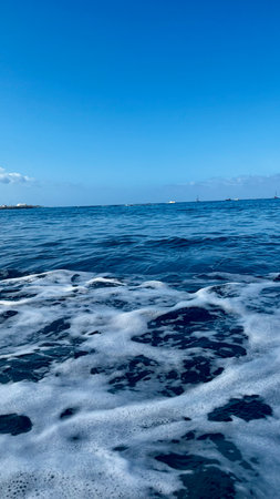 Atlantic waves hit the sandy beach. Black sand and blue sky. Vertical image. Costa Adeje, Spain