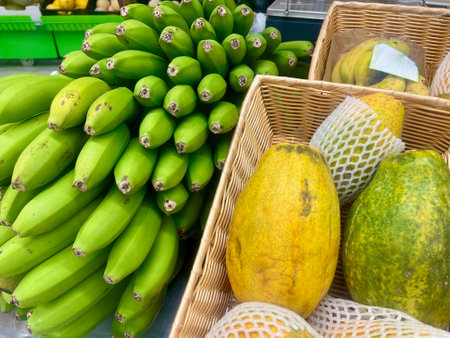 Showcase with fresh organic vegetables fruits in supermarket. Green bananas and yellow papayaの写真素材
