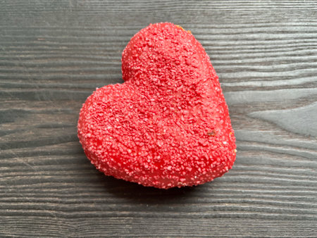 A heart-shaped donut with pink sprinkles. Lying on a black wooden surfaceの写真素材