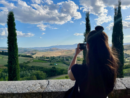 Attractive dark-haired girl takes picture of a beautiful Tuscan valley with her smartphoneの写真素材