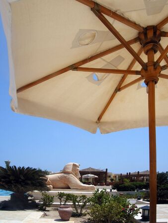 Sunshade and statue of sphinx close to swimming poolの写真素材