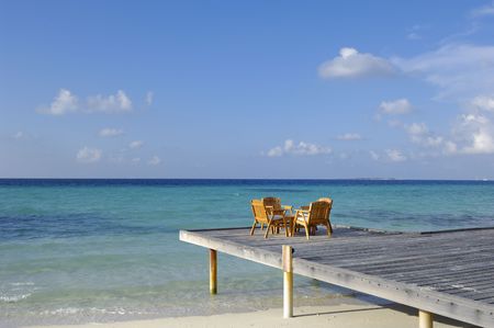 Chairs and table on deck by beach, Kuramathi island, Maldivesの写真素材