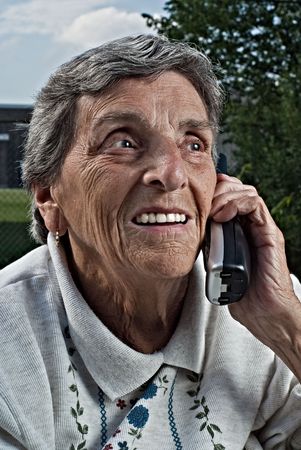 An elderly senior woman smiles while talking on a cordless phone.