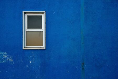 A small window on a blue, rough and worn exterior wall.の写真素材