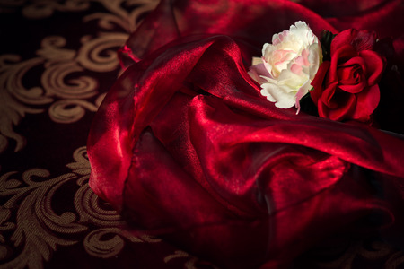 A white and red silk rose and carnation sits atop a wadding of luxurious, flowing silk material.