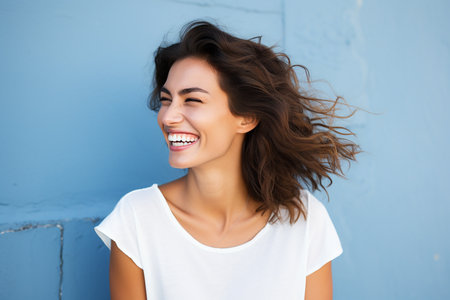 Portrait of a beautiful young woman laughing and looking away against blue wallの素材