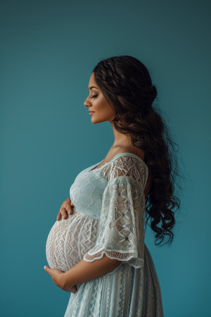 pregnant woman in lace dress touching her belly isolated on blueの素材