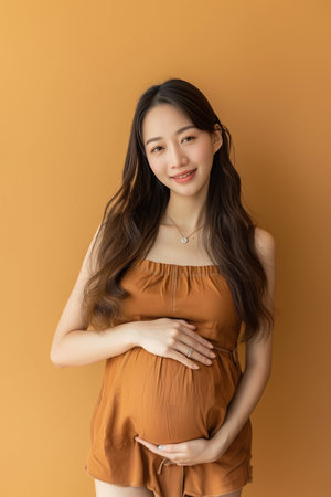 Beautiful asian pregnant woman touching her belly isolated on orange backgroundの素材