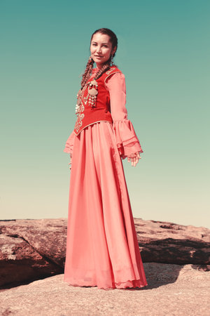 Portrait of a beautiful young woman in a red dress on the rocks Kazakh woman and man in national costumesの写真素材