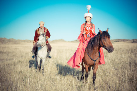 Young couple in historical clothes on horseback in the steppe. Kazakh woman and man in national costumesの写真素材