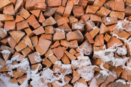 Wall of firewood, background of dry chopped firewood covered with snow. Alternative fuel concept.