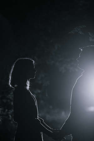 Young couple enjoying time in the forest during nighttime. Silhouette picture of the couple looking at each other in the forest with backlight.の写真素材
