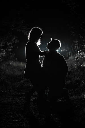 Young couple enjoying time in the forest during nighttime. Silhouette picture of the couple looking at each other in the forest with backlight.の写真素材