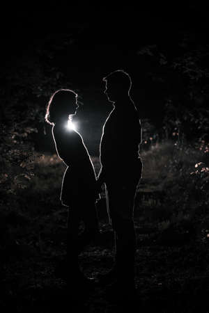 Young couple enjoying time in the forest during nighttime. Silhouette picture of the couple looking at each other in the forest with backlight.の写真素材