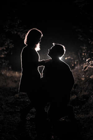Young couple enjoying time in the forest during nighttime. Silhouette picture of the couple looking at each other in the forest with backlight.の写真素材