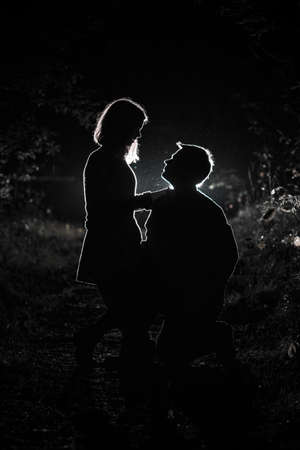 Young couple enjoying time in the forest during nighttime. Silhouette picture of the couple looking at each other in the forest with backlight.の写真素材