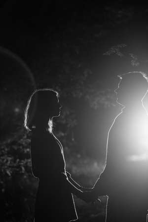 Young couple enjoying time in the forest during nighttime. Silhouette picture of the couple looking at each other in the forest with backlight.の写真素材