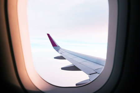 Airplane wing on a flight above the clouds during the sunsetの写真素材