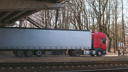 Red truck drives under a bridge on a sunny day near the railway tracksの写真素材