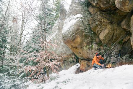 hiker prepares food on fire, while snowfall in the woods, survivalの写真素材