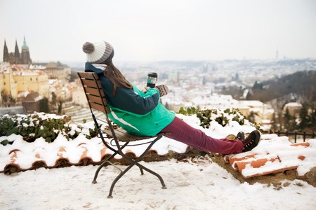 Not recognizable girl who sits on a chair and drinks from a cup, enjoys a wonderful sunset against the background of the city of Pragueの写真素材