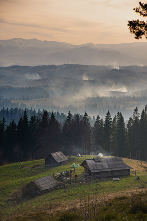Sunrise above the high mountain foggy valley with old wooden houses on a hill in a mountain forestの写真素材