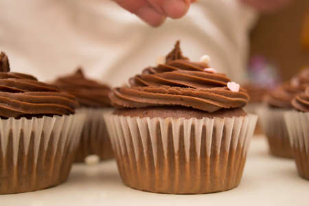 Bakers fingers throwing sprinkles over chocolate cupcakeの写真素材