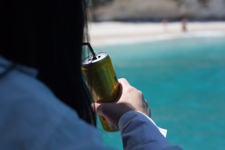 Woman drinking beer from a can on the beach. Selective focus.