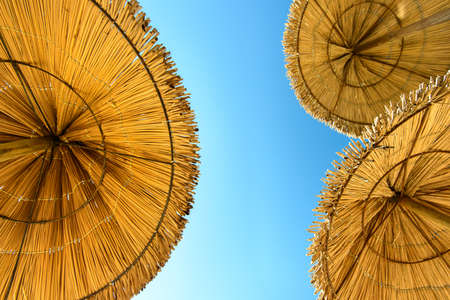 view of three thatched umbrellas and sky from person, who lays in the sunの写真素材