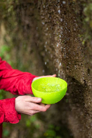 Person gathering water into green cup in environmental conditionsの写真素材