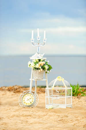 White vintage decor for photosession on the beach in the morning: flowers, candle holder, the birdcage and clockの写真素材
