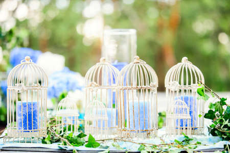 white vintage decoration: birdcages with blue candles on wedding table with green leaves on nature backgroundの写真素材