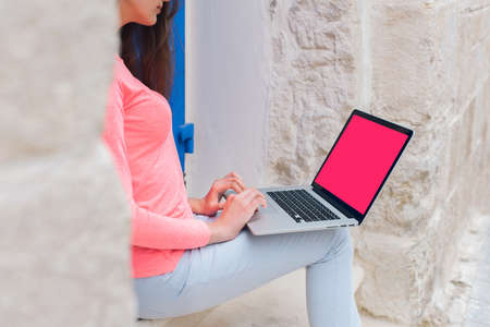 Beautiful young blonde female student using portable laptop computer while sitting on the stairs in...