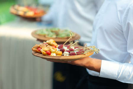 Catering - food, plate and hand. Waiters carrying plates with sweets, croissants and fruits at a...
