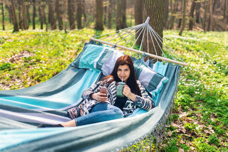 Happy healthy eating girl drinking green smoothie detox outdoors in hammock. Woman on weight loss diet vegan nutrition cleanse.の写真素材