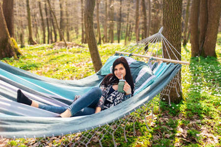 Happy healthy eating girl drinking green smoothie detox outdoors in hammock. Woman on weight loss diet vegan nutrition cleanse.の写真素材